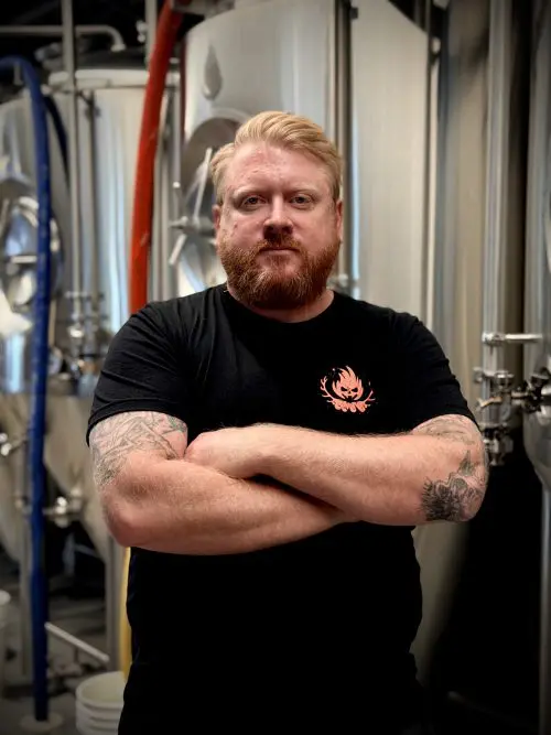 Matt wearing a black shirt and crossing his arms in front of some fermentation tanks