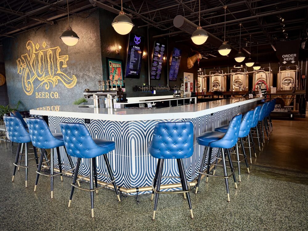Xul downtown taproom features a white bar top and blue leather chairs next to a logo wall