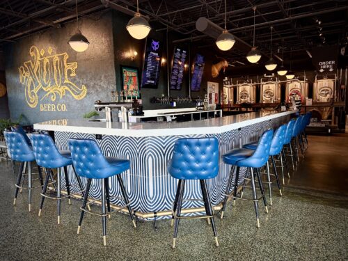 Xul downtown taproom features a white bar top and blue leather chairs next to a logo wall
