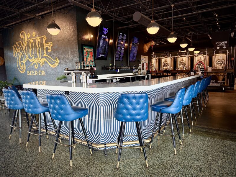 Xul downtown taproom features a white bar top and blue leather chairs next to a logo wall