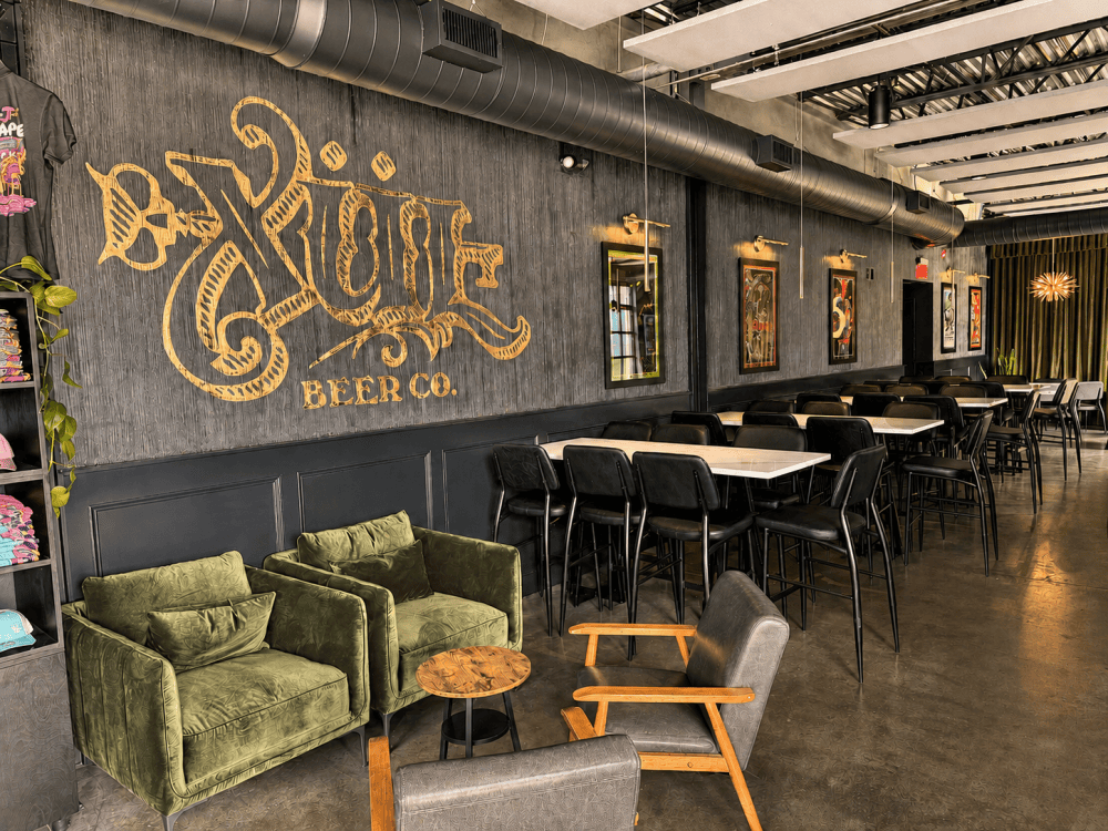 Xul Beer logo wall and lounge seating inside the West Nashville taproom in The Nations, featuring green velvet chairs and dark interior finishes.