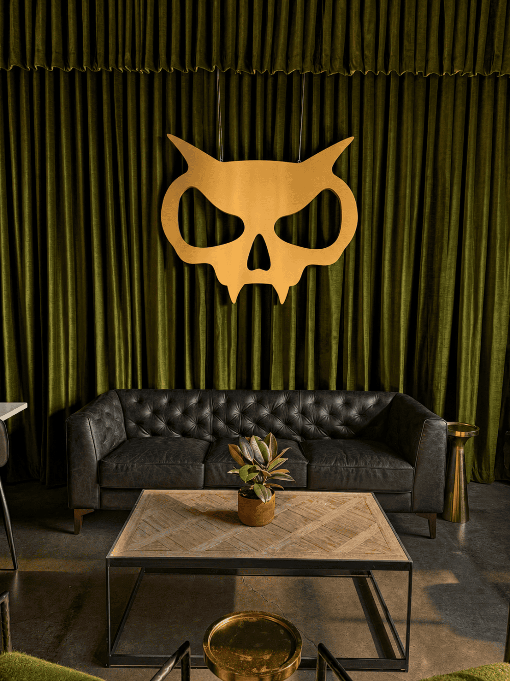 Lounge area at Xul Beer Company’s Nations Taproom in Nashville, featuring a black leather sofa, green velvet curtains and a gold skull emblem.